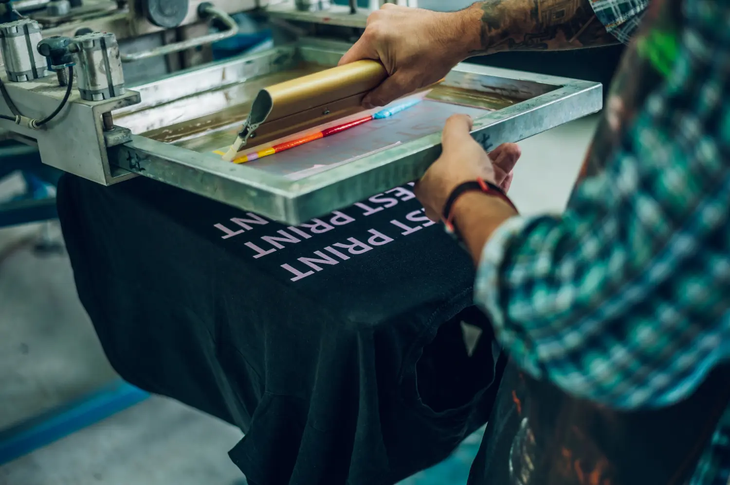 PB-Werbeartikel, Textilien mit Druck oder Stick,  Männlicher Arbeiter drückt Farbe auf einen Rahmen, während er die Druckmaschine in einer Werkstatt benutzt