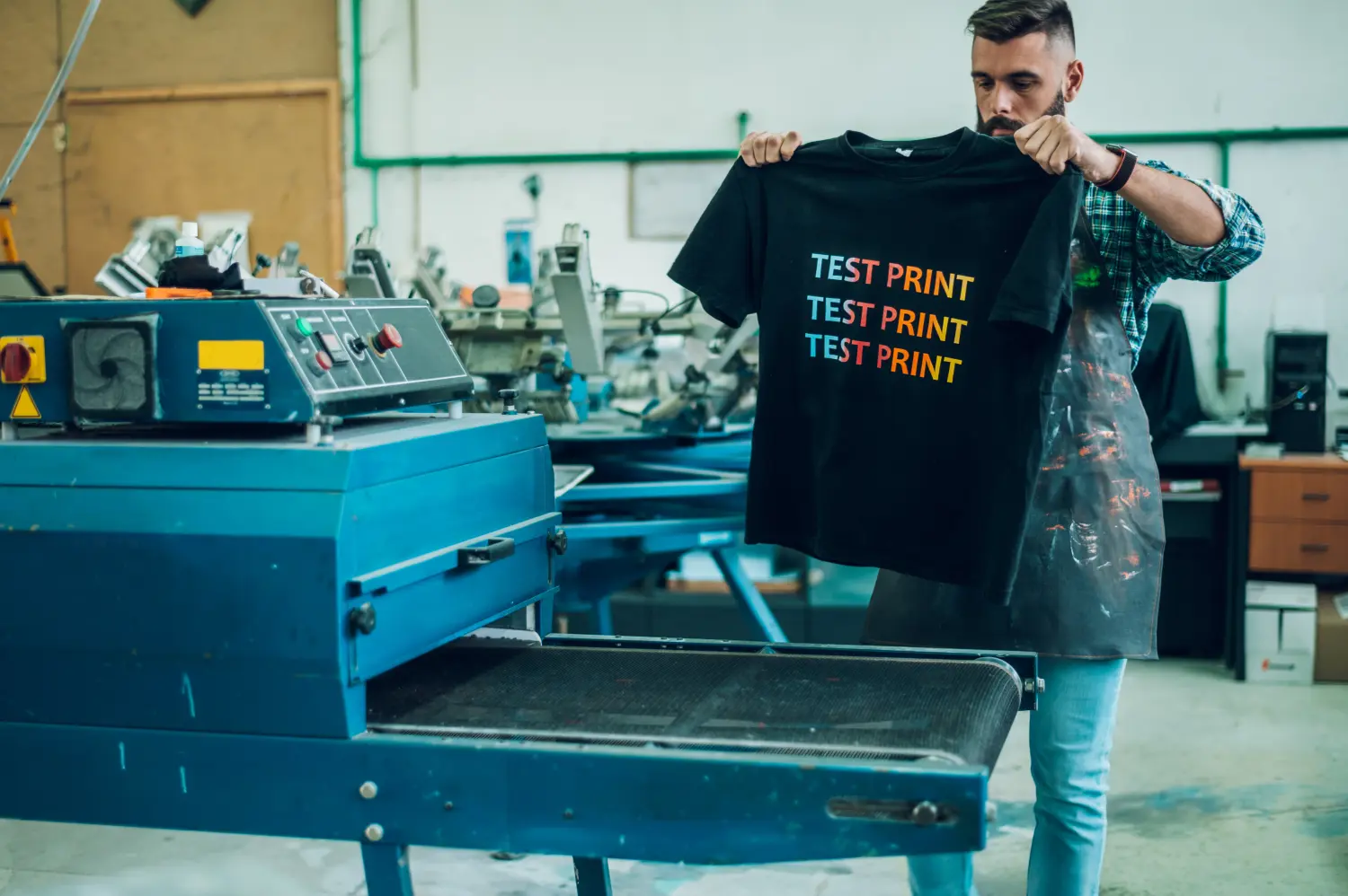 PB-Werbeartikel, Textilien mit Druck oder Stick, Männlicher Arbeiter benutzt einen Trockenofen für T-Shirts in einer Werkstatt